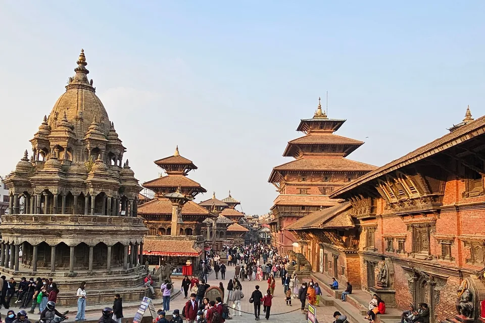 People walking between the stone temples and brick palace buildings of Patan Durbar Square.